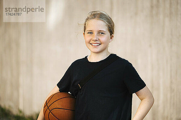 Porträt eines lächelnden Mädchens mit Basketball an der Wand