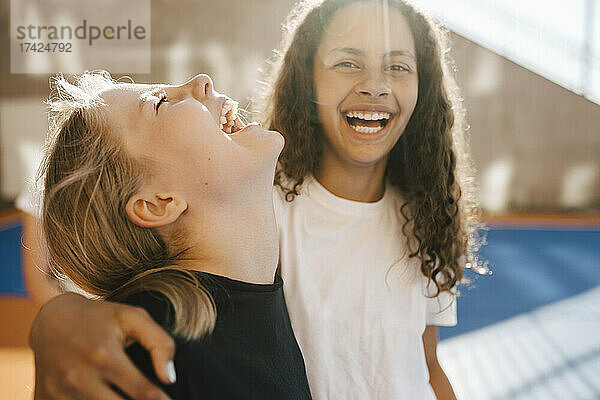 Fröhliche Freundinnen lachen am Basketballplatz an einem sonnigen Tag