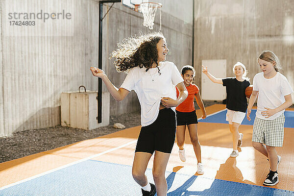 Glückliche multiethnische Mädchen spielen auf einem Basketballplatz an einem sonnigen Tag