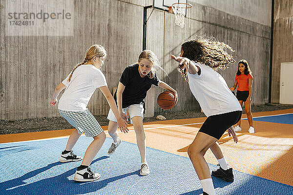 Freundinnen verteidigen ein Mädchen beim Basketballspielen während eines Wettbewerbs auf einem Sportplatz