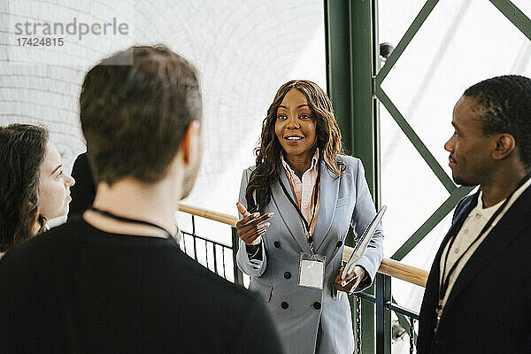 Geschäftsfrau gestikuliert während eines Gesprächs mit männlichen und weiblichen Kollegen bei einer Networking-Veranstaltung
