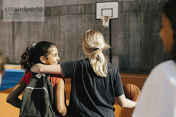 Blondes Mädchen mit Arm um Freundin beim Gehen im Basketballplatz