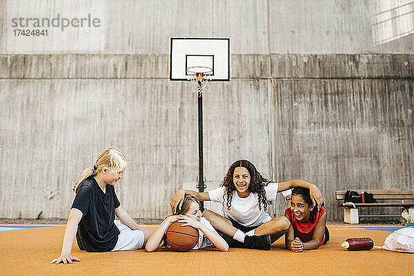 Porträt eines Mädchens  das mit seinen Freundinnen auf dem Basketballplatz sitzt
