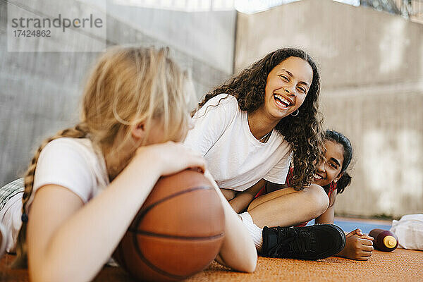 Porträt eines lachenden Mädchens  das mit Freundinnen auf dem Basketballplatz sitzt