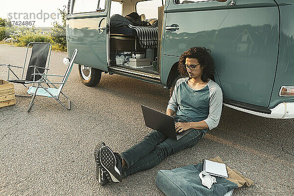 Mann mit Laptop  der an einem Campingwagen sitzt