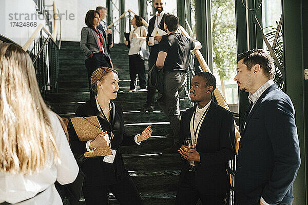 Weibliche Unternehmerin diskutiert mit männlichen Kollegen  während sie an einer Treppe im Kongresszentrum steht