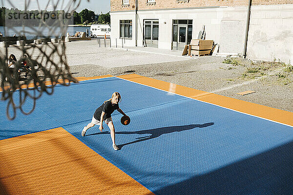 Hoher Winkel Blick auf Mädchen dribbelnden Ball auf Basketballplatz an einem sonnigen Tag