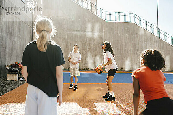 Multi-ethnische Freundinnen spielen Basketball auf einem Sportplatz an einem sonnigen Tag