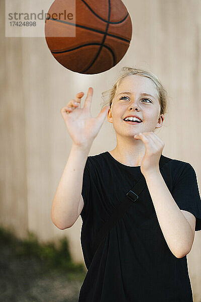 Lächelndes Mädchen spielt mit Ball auf dem Basketballplatz