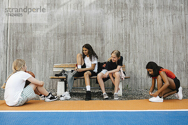 Multiethnische Freundinnen unterhalten sich auf einer Bank am Basketballplatz