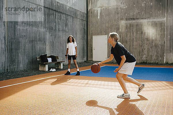 Vorpubertäres Mädchen dribbelt Basketball  während sie mit einer Freundin im Hof spielt