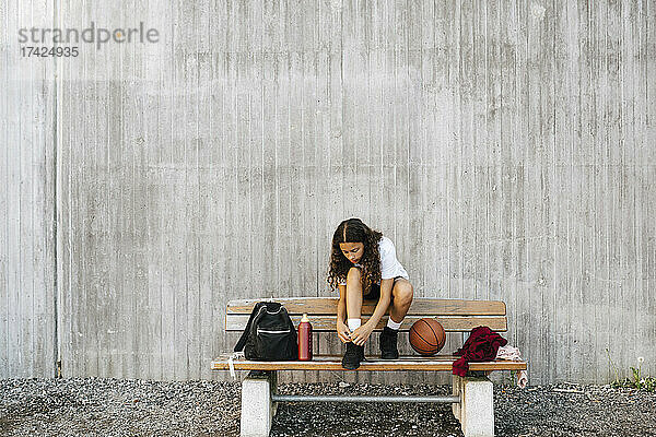 Eine Basketballspielerin bindet ihre Schnürsenkel  während sie auf einer Bank an der Wand sitzt