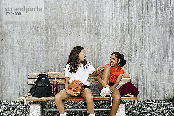 Glückliche vorpubertäre Mädchen  die sich auf einer Bank an der Wand sitzend unterhalten