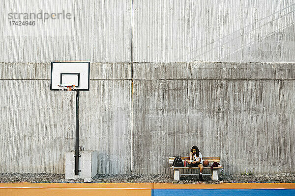 Mädchen bindet Schnürsenkel  während sie auf einer Bank am Basketballplatz sitzt