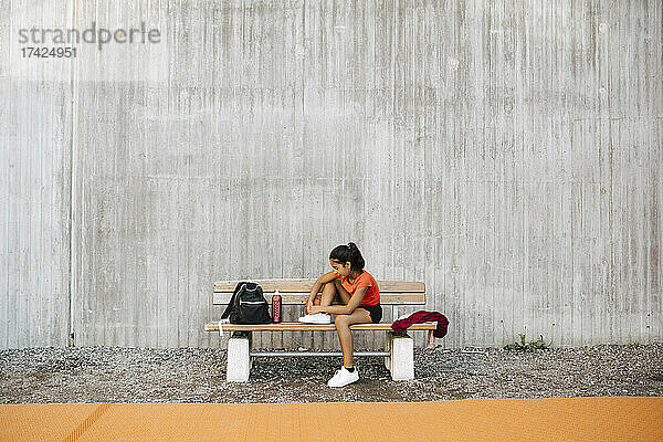 Mädchen bindet Schnürsenkel an der Wand des Sportplatzes