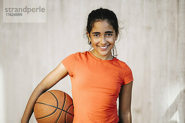 Porträt eines lächelnden Mädchens mit Basketball an der Wand