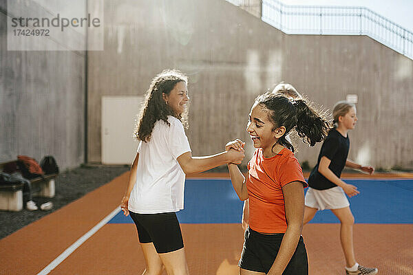 Glückliche Freundinnen halten sich die Hände  während sie auf dem Basketballplatz spielen