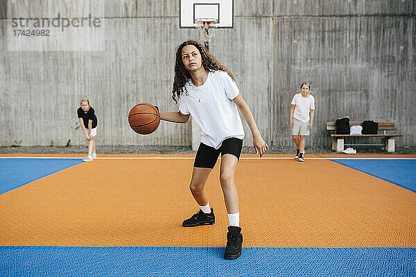 Vorpubertäres Mädchen  das wegschaut  während es auf dem Platz Basketball übt
