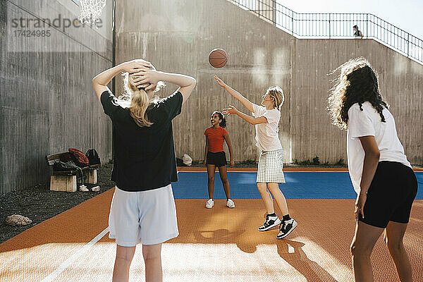 Mädchen wirft Basketball gegen den Reifen  während sie mit Freunden auf dem Platz spielt