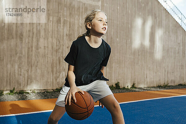 Vorpubertäres Mädchen  das beim Basketballspielen auf dem Sportplatz wegschaut