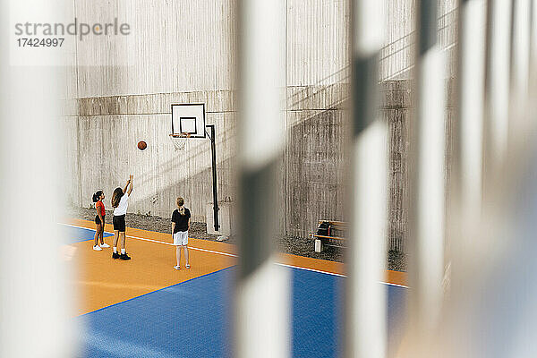 Freundinnen spielen Basketball  gesehen durch das Geländer am Sportplatz