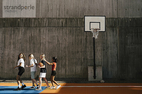 Freundinnen  die in einer Reihe an der Wand des Basketballplatzes laufen