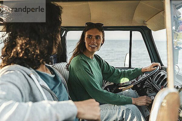 Frau im Gespräch mit einem männlichen Freund  während sie in einem Van am Meer sitzt