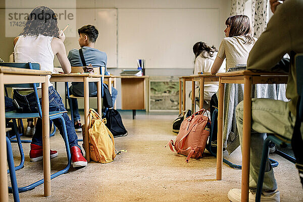 Eine gemischtrassige Gruppe von Schülern sitzt am Schreibtisch im Klassenzimmer