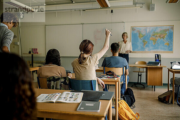 Teenager-Mädchen hebt die Hand im Klassenzimmer der High School