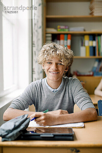 Lächelnder blonder Jugendlicher am Schreibtisch im Klassenzimmer