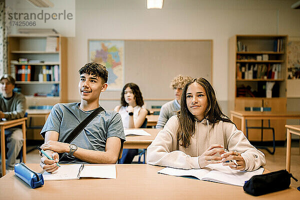 Lächelnde Mittelschüler mit Buch und Stift  die in einem beleuchteten Klassenzimmer lernen