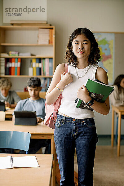 Porträt eines Mädchens im Teenageralter mit Buch und Rucksack im Klassenzimmer