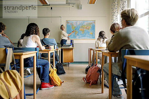 Lehrerin unterrichtet Mädchen und Jungen im Klassenzimmer über Landkarten