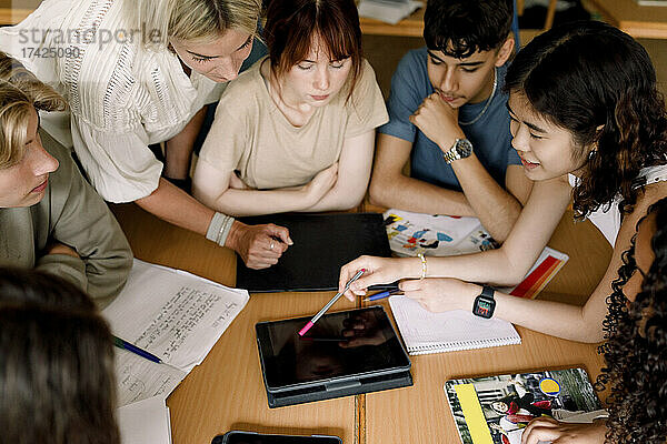 Multirassische Mädchen und Jungen mit einer Lehrerin  die über ein digitales Tablet im Klassenzimmer lernen