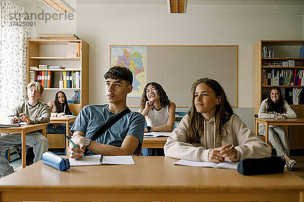 Lächelnde Studenten  die am Schreibtisch im Klassenzimmer lernen