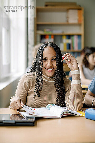 Porträt eines lächelnden Mädchens mit Buch auf dem Schreibtisch in der High School