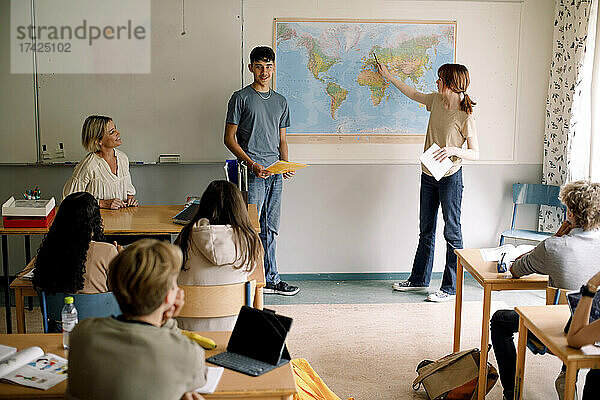 Teenager und Mädchen erklären über Weltkarte im Klassenzimmer