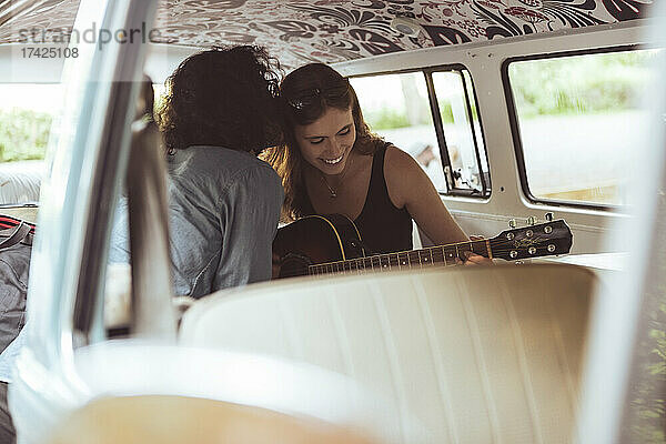 Lächelnde Frau spielt Gitarre  während ihr männlicher Freund sie im Campingbus küsst