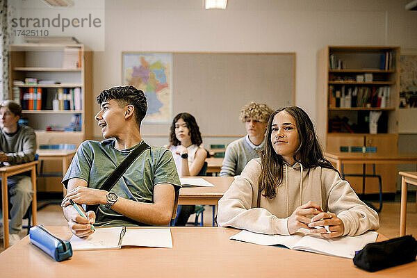 Jungen und Mädchen sitzen mit Buch auf dem Schreibtisch im Klassenzimmer