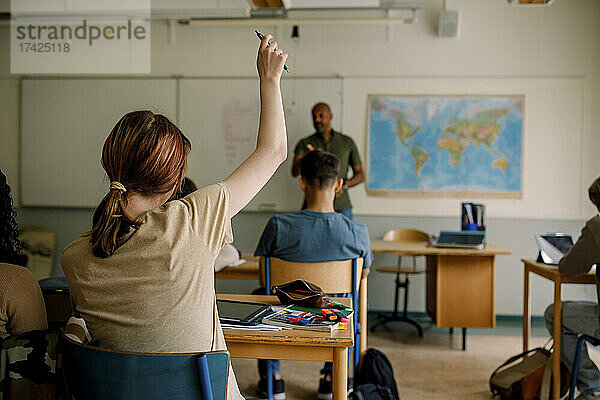 Jugendlicher Schüler hebt die Hand beim Lernen im Klassenzimmer der High School