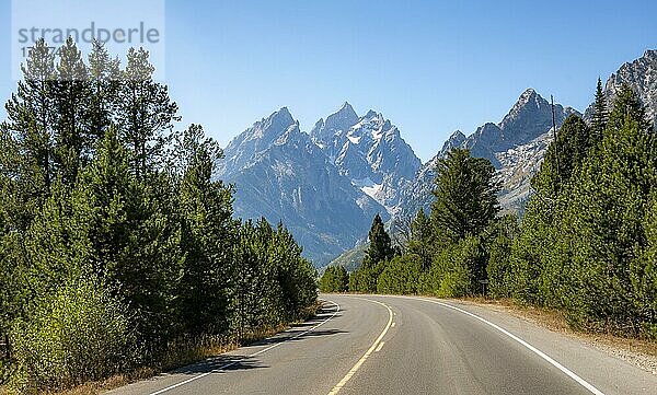 Landstraße durch Wald  hinten schroffe Berggipfel  Grand Teton  Mount Teewinot und Mount St. John  Teton Range Gebirgszug  Grand Teton National Park  Wyoming  USA  Nordamerika