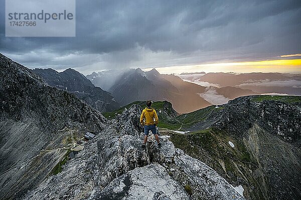 Wanderer am Gipfel der Westlichen Törlspitze  hinten wolkenverhangene Berge bei Sonnenuntergang mit dramatischem Licht  Blick auf Frauenalpl  Wettersteingebirge  Garmisch Partenkirchen  Bayern  Deutschland  Europa