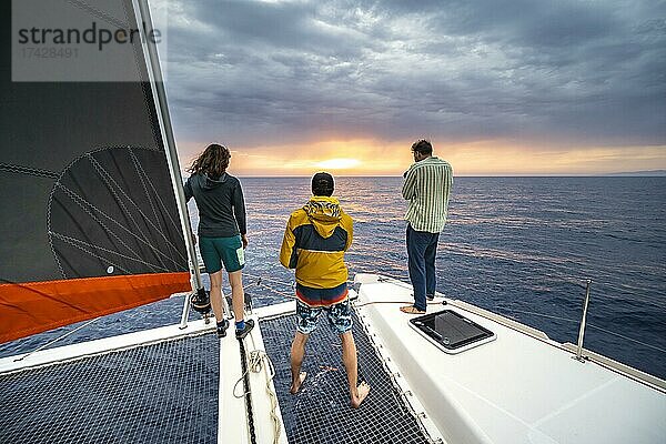 Junge Frau und zwei junge Männer stehen auf Katamaran und blicken in den Sonnenuntergang  Rhodos  Dodekanes  Griechenland  Europa
