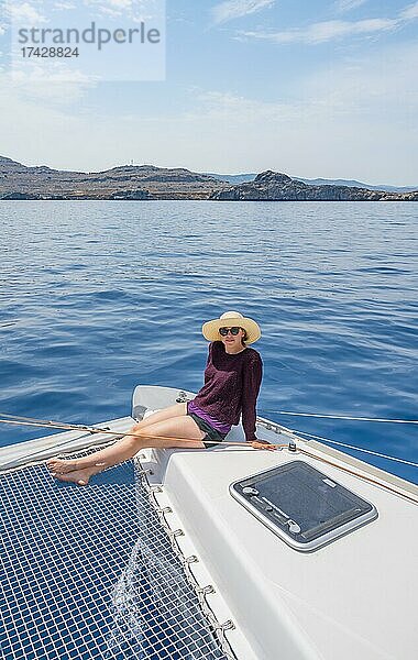 Junge Frau mit Hut sitzt auf Deck am Netz eines Segel-Katamaran  Segeltörn  Rhodos  Dodekanes  Griechenland  Europa