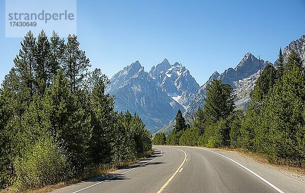 Landstraße durch Wald  hinten schroffe Berggipfel  Grand Teton  Mount Teewinot und Mount St. John  Teton Range Gebirgszug  Grand Teton National Park  Wyoming  USA  Nordamerika