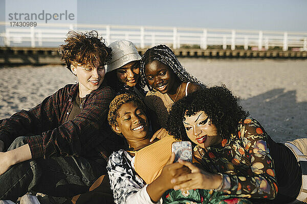 Lächelnde multirassische Freunde mit Mobiltelefon am Strand