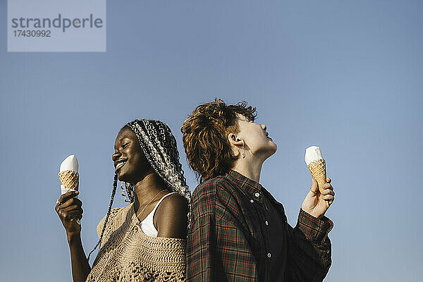 Lächelnder Teenager und junge Frau halten Eistüten gegen den klaren Himmel