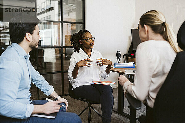 Mittlere erwachsene Geschäftsfrau  die mit männlichen und weiblichen Kollegen in einem kreativen Büro diskutiert
