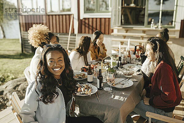 Lächelnde junge Frau sitzt am Esstisch mit Freundinnen an einem sonnigen Tag