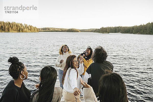 Glückliche Freundinnen tanzen am Seeufer gegen den klaren Himmel